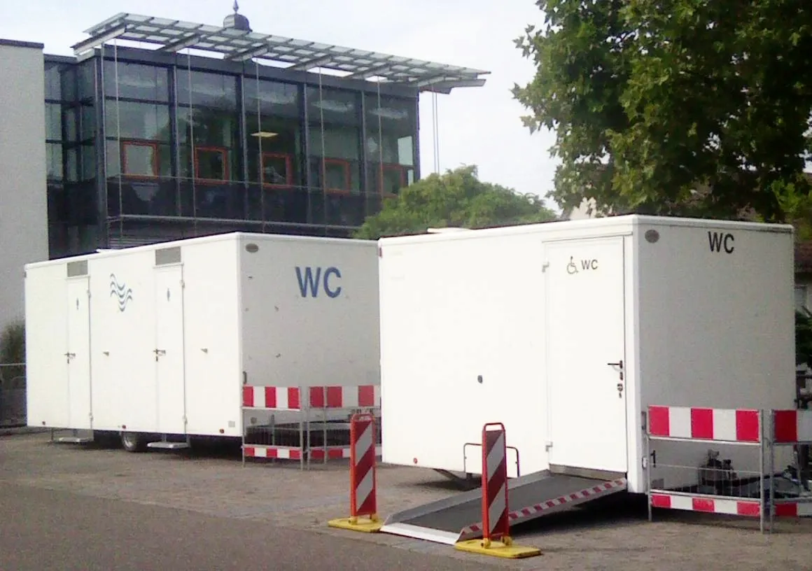 Two white restroom trailers, one with a ramp up to an accessible restroom door